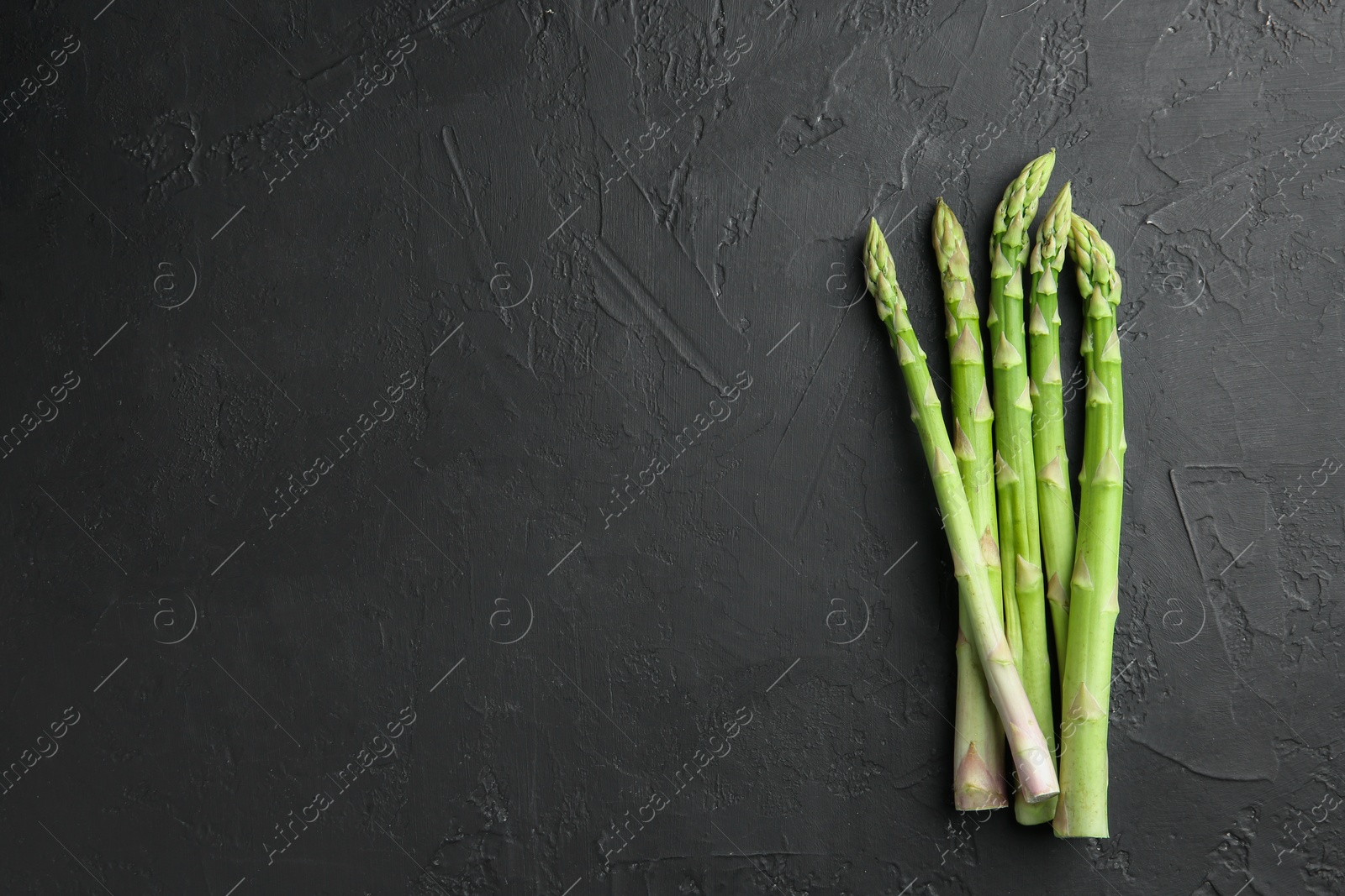 Photo of Fresh green asparagus stems on gray textured table, top view. Space for text