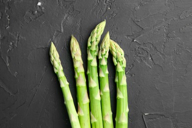 Photo of Fresh green asparagus stems on gray textured table, top view