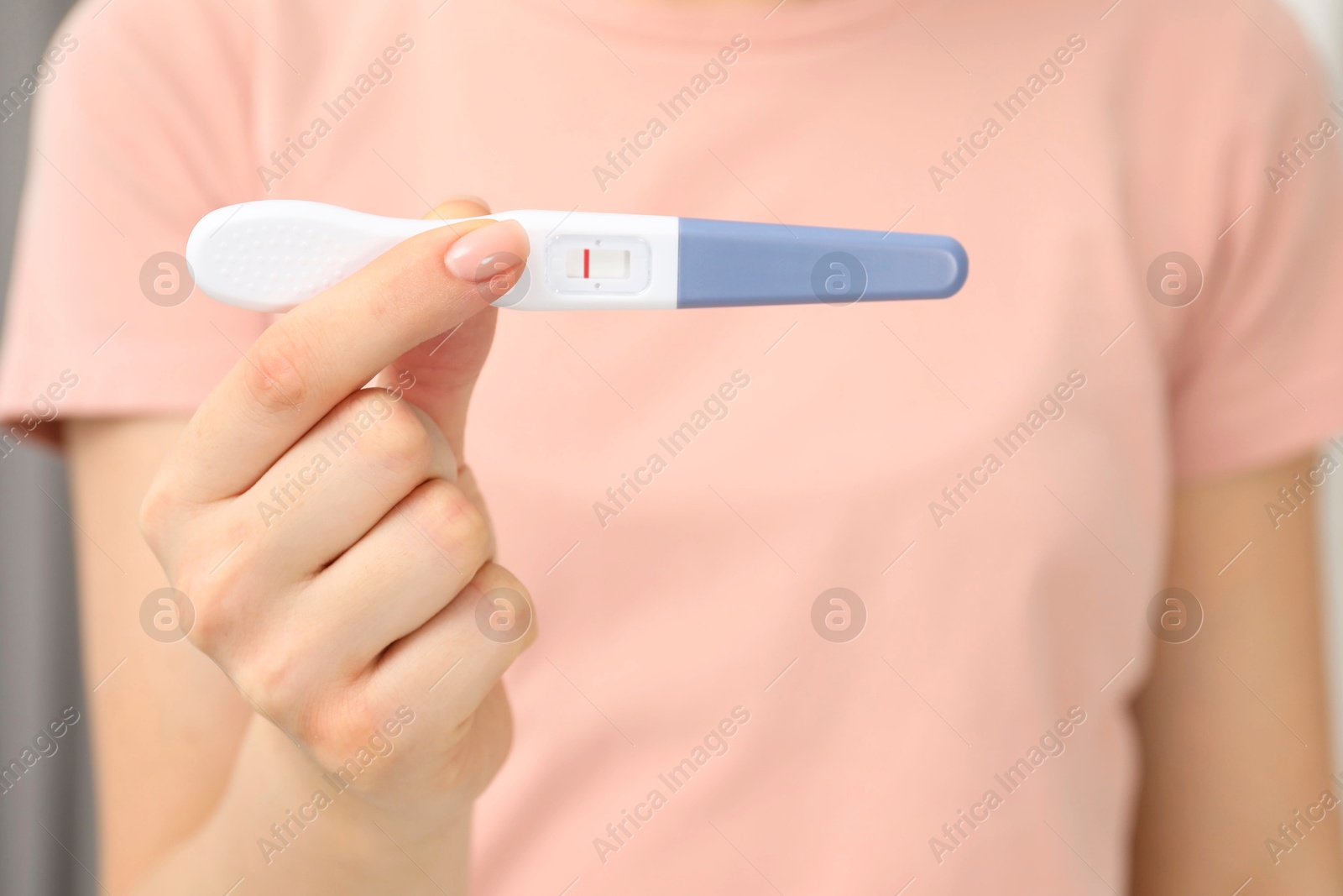 Photo of Woman holding negative pregnancy test indoors, closeup view