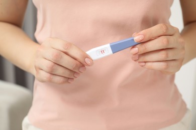 Woman holding positive pregnancy test indoors, closeup view