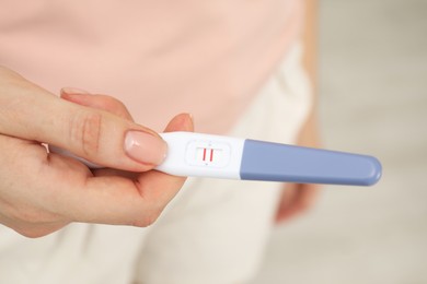 Woman holding positive pregnancy test indoors, closeup view