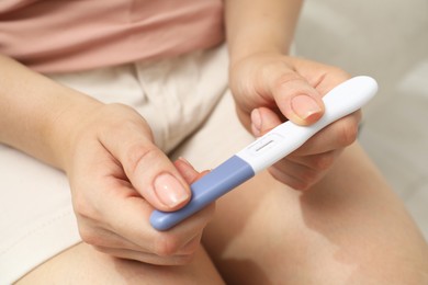 Photo of Woman holding pregnancy test indoors, closeup view