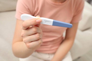 Woman holding pregnancy test indoors, closeup view