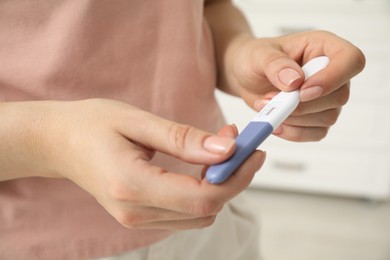 Photo of Woman holding pregnancy test indoors, closeup view