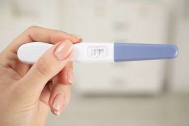 Photo of Woman holding positive pregnancy test indoors, closeup view