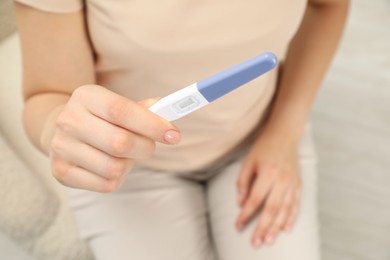 Photo of Woman holding pregnancy test indoors, closeup view