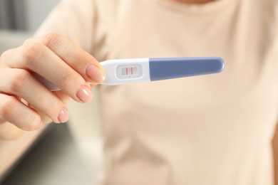 Photo of Woman holding positive pregnancy test indoors, closeup view