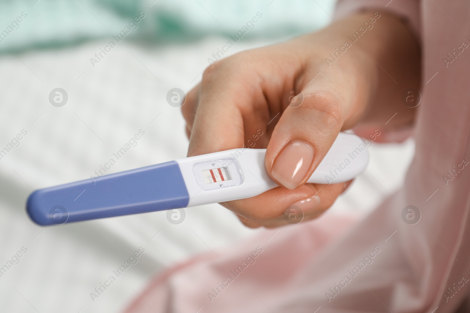 Photo of Woman holding positive pregnancy test indoors, closeup view