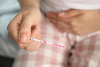 Photo of Woman holding positive pregnancy test indoors, closeup view