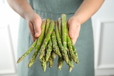 Photo of Woman with fresh asparagus stems indoors, closeup