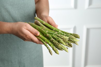 Woman with fresh asparagus stems indoors, closeup