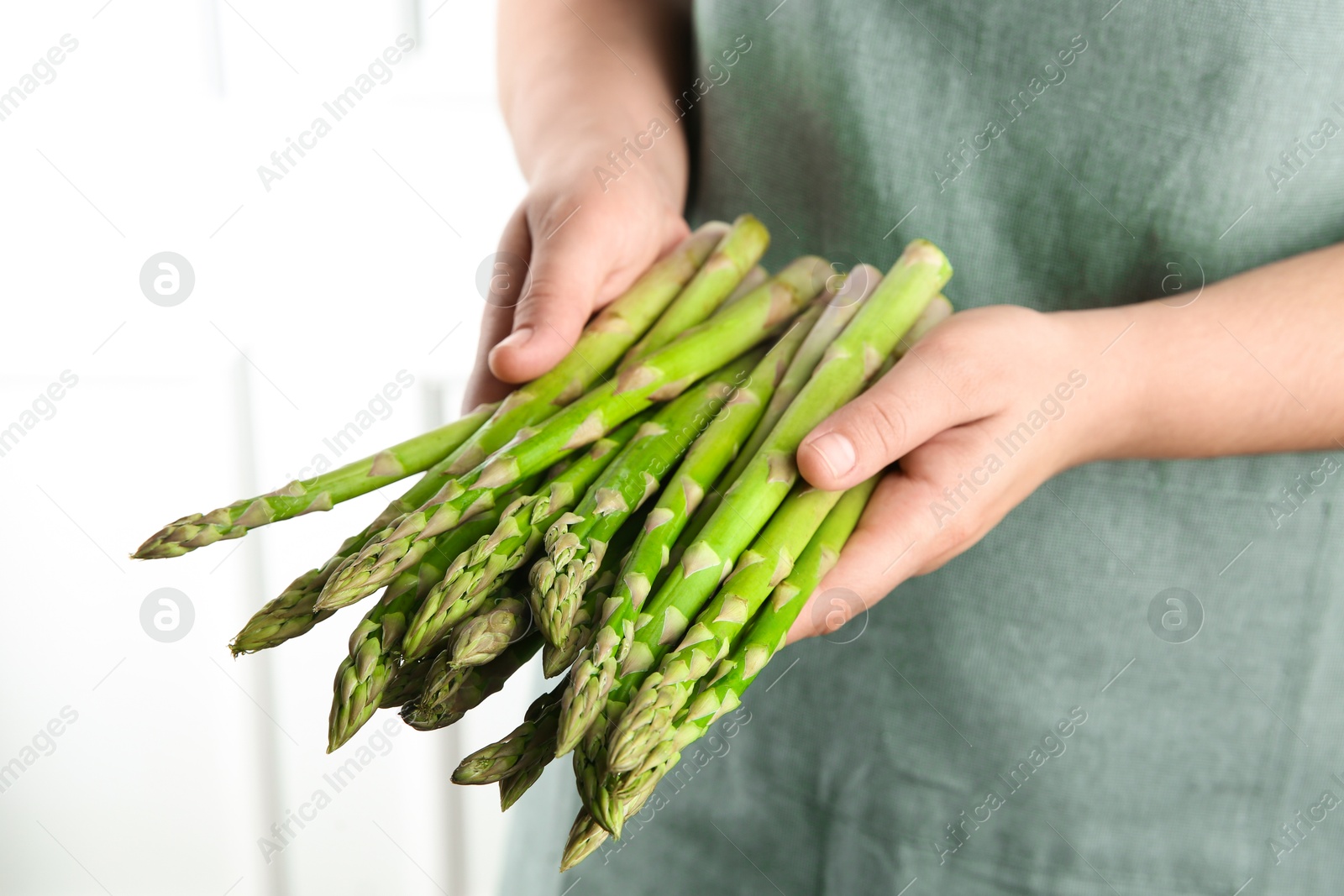 Photo of Woman with fresh asparagus stems indoors, closeup