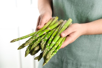 Woman with fresh asparagus stems indoors, closeup