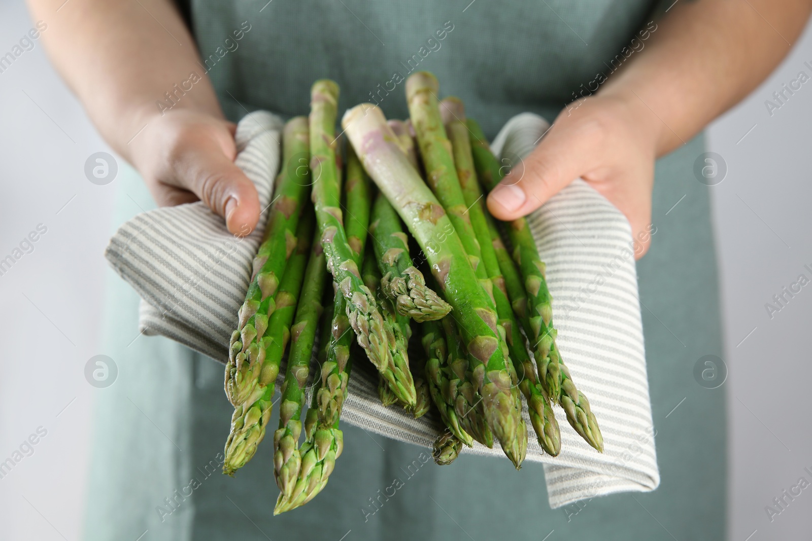 Photo of Woman with fresh asparagus stems on light grey background, closeup