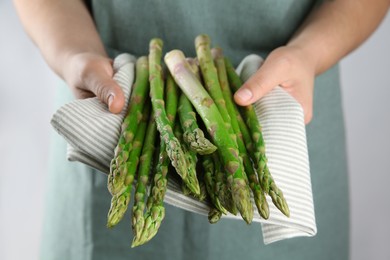 Photo of Woman with fresh asparagus stems on light grey background, closeup