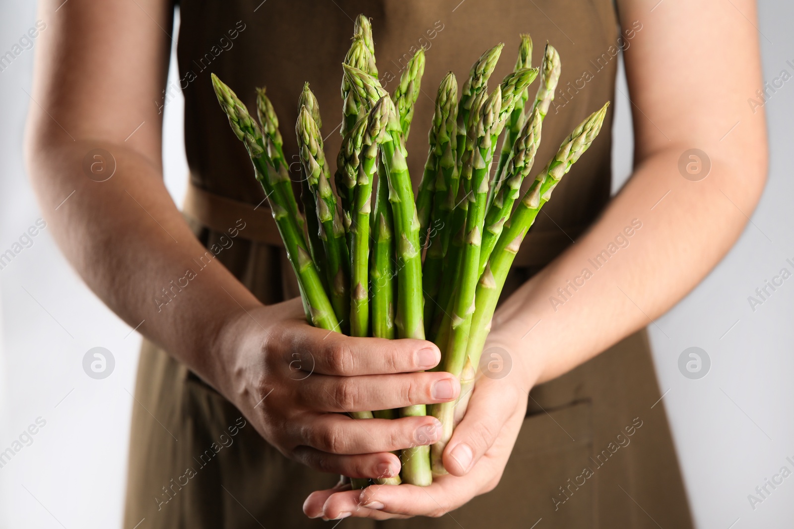 Photo of Woman with fresh asparagus stems on light grey background, closeup