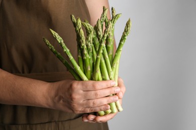 Woman with fresh asparagus stems on light grey background, closeup. Space for text