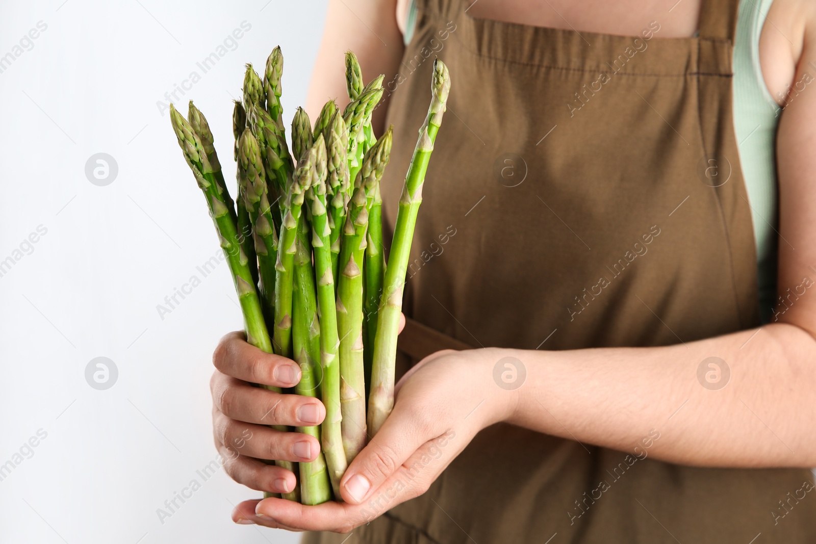 Photo of Woman with fresh asparagus stems on light grey background, closeup