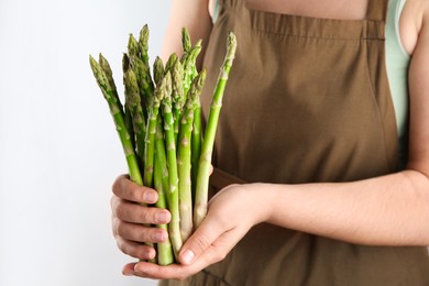 Photo of Woman with fresh asparagus stems on light grey background, closeup