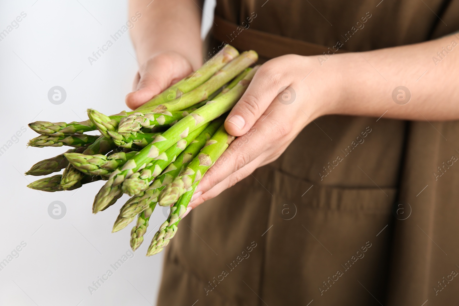 Photo of Woman with fresh asparagus stems on light grey background, closeup