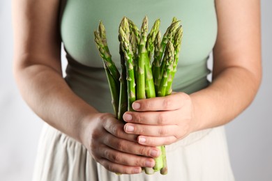 Photo of Woman with fresh asparagus stems on light grey background, closeup