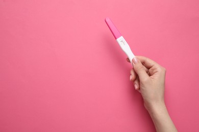 Photo of Woman holding pregnancy test on pink background, top view. Space for text