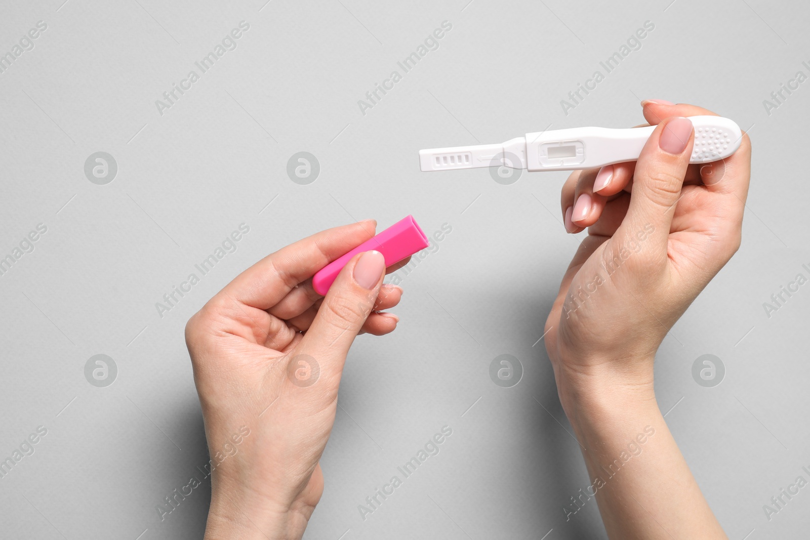 Photo of Woman holding pregnancy test on light grey background, top view