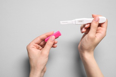 Woman holding pregnancy test on light grey background, top view