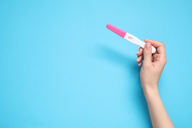 Photo of Woman with pregnancy test on light blue background, top view. Space for text