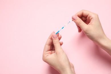 Woman holding pregnancy test on pink background, closeup. Space for text