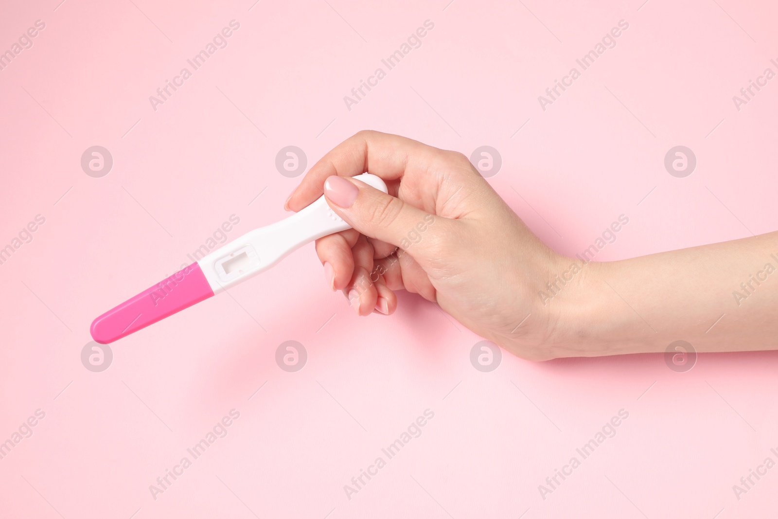 Photo of Woman holding pregnancy test on pink background, closeup