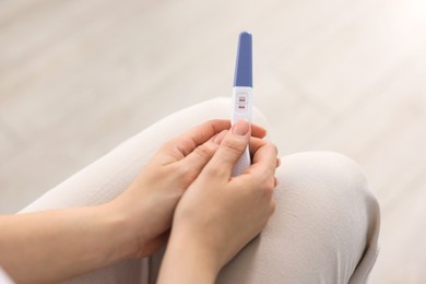 Photo of Woman holding pregnancy test in room, closeup