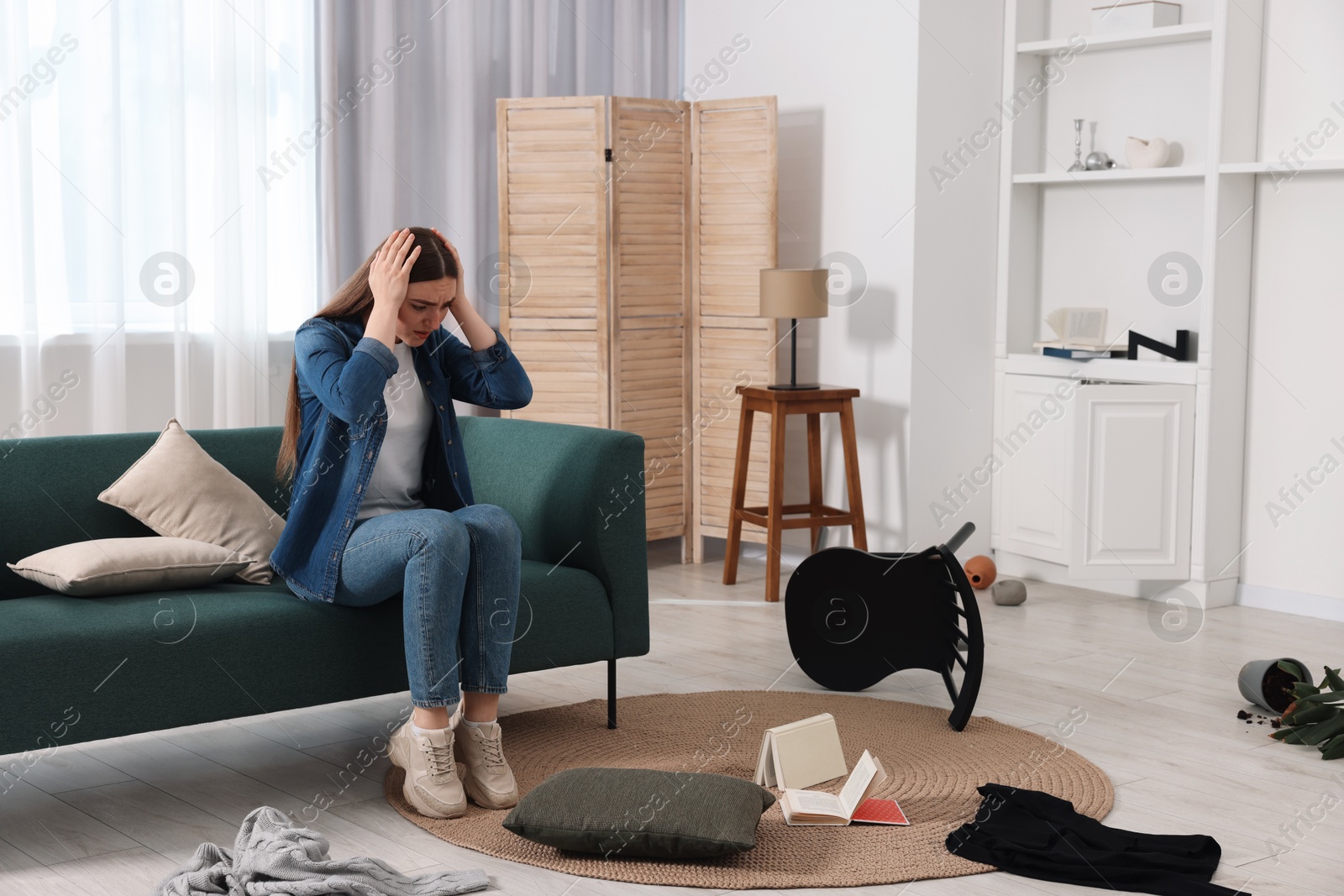 Photo of Desperate woman sitting on sofa in messy living room after robbery