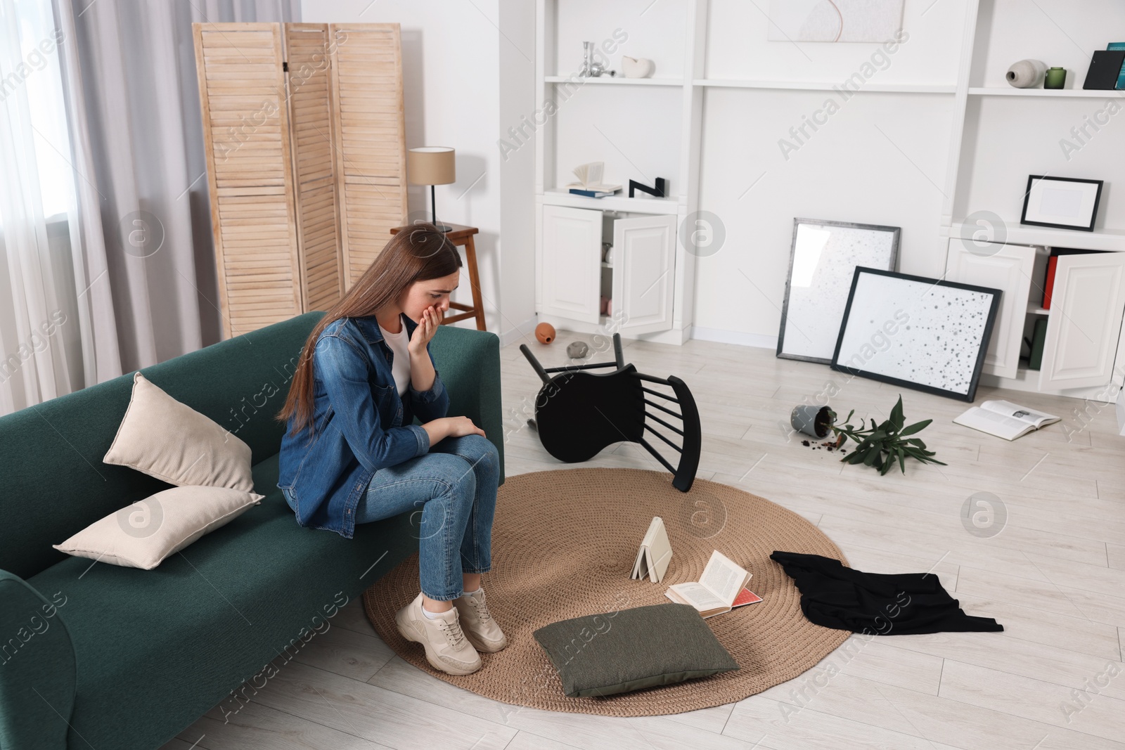 Photo of Desperate woman sitting on sofa in messy living room after robbery