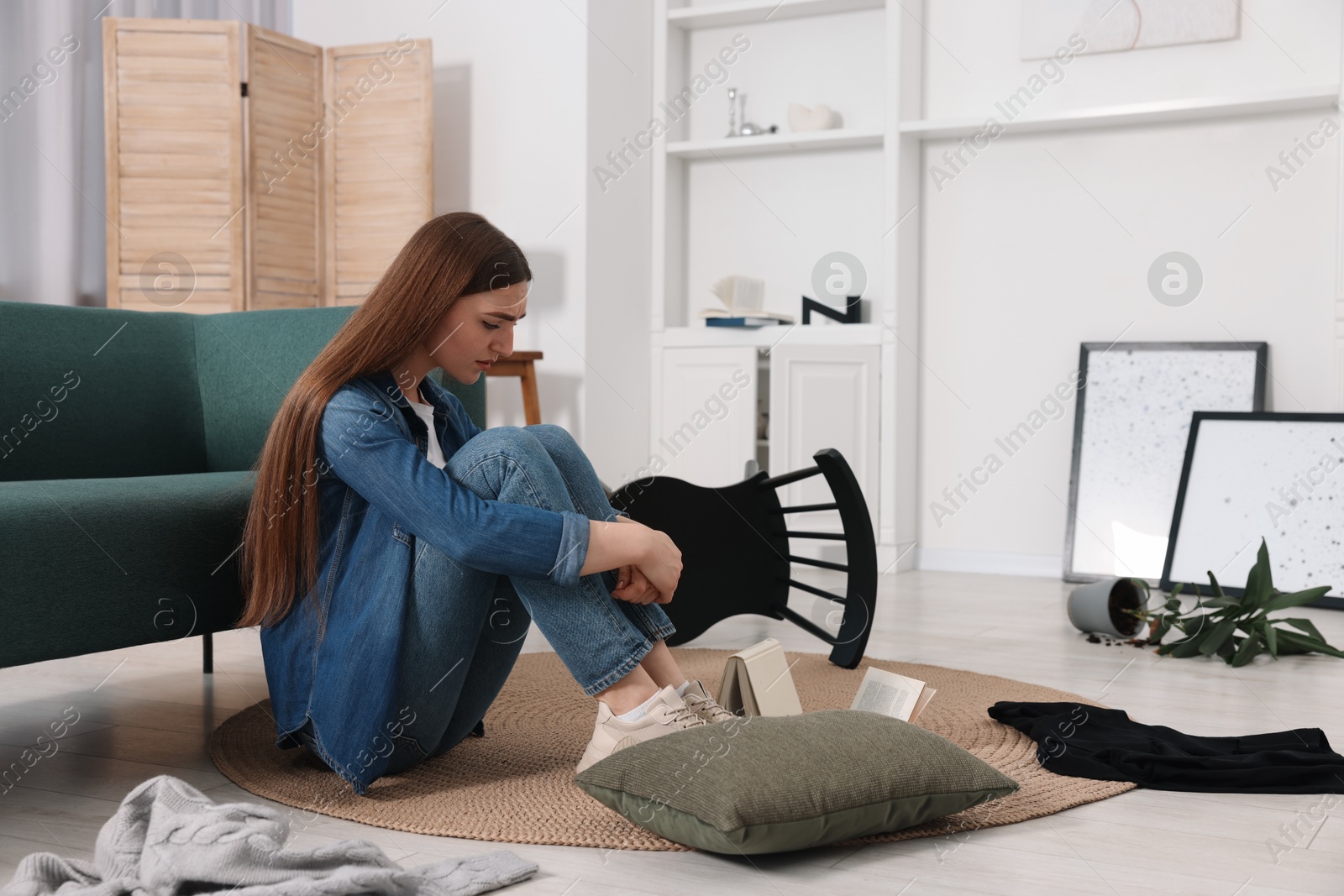 Photo of Desperate woman sitting on floor in messy living room after robbery