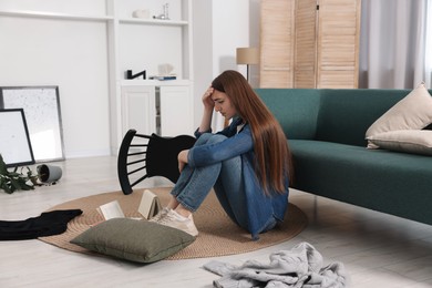 Photo of Desperate woman sitting on floor in messy living room after robbery