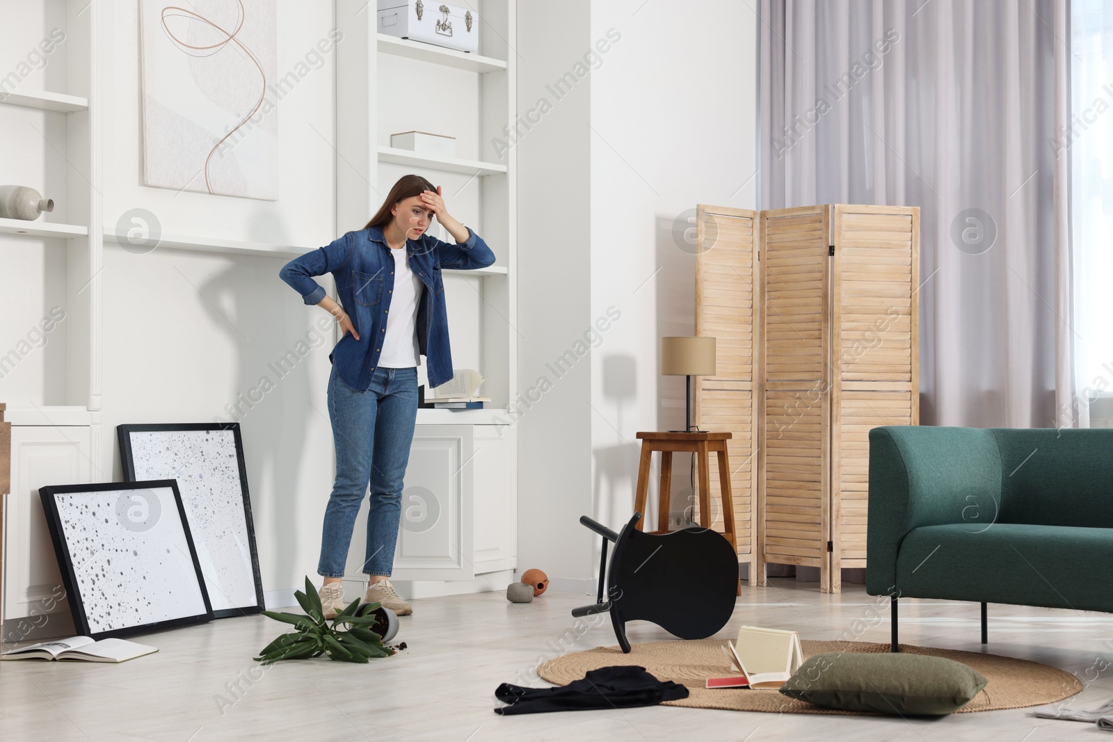 Photo of Desperate woman standing in messy living room after robbery