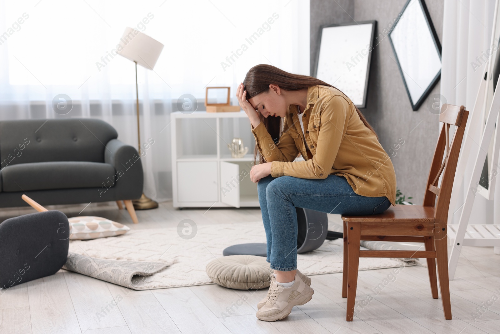 Photo of Desperate woman sitting on chair in messy living room after robbery