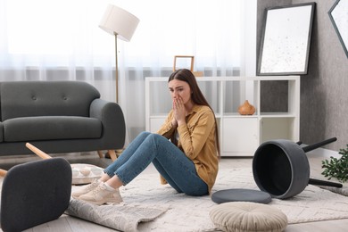 Photo of Desperate woman sitting on floor in messy living room after robbery