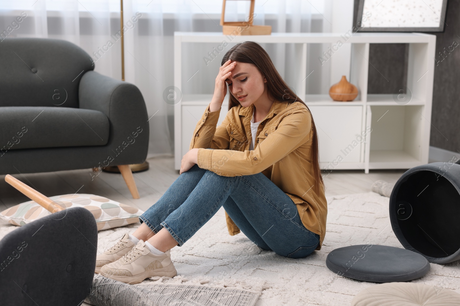 Photo of Desperate woman sitting on floor in messy living room after robbery