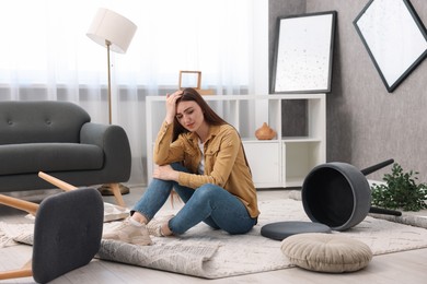 Desperate woman sitting on floor in messy living room after robbery