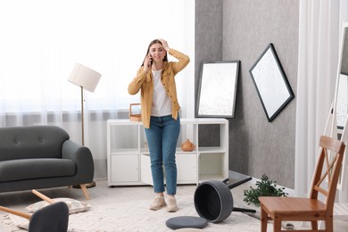 Desperate woman talking on smartphone in messy living room after robbery