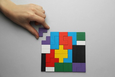 Photo of Woman playing with colorful wooden puzzle pieces on light grey background, top view