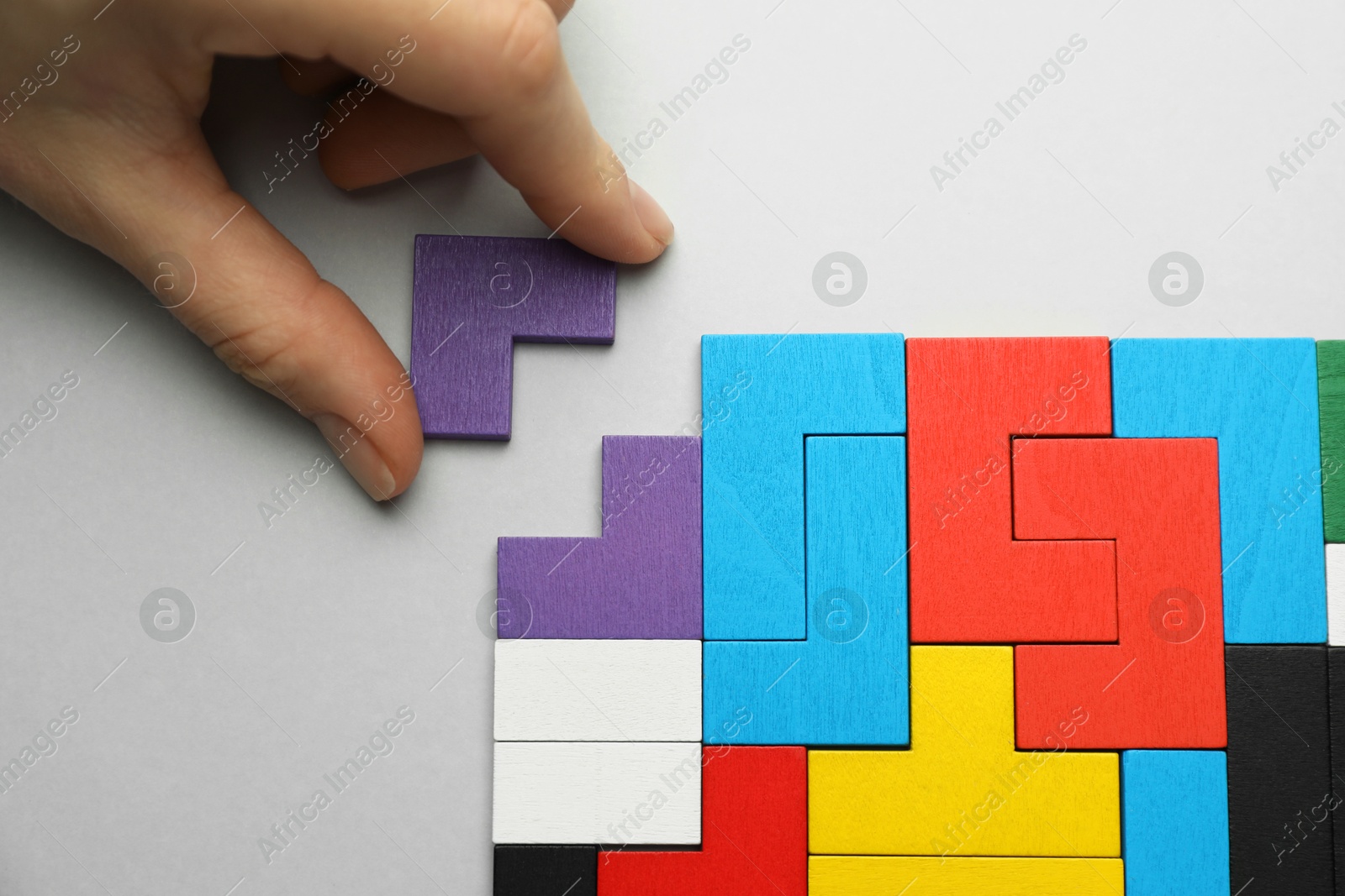 Photo of Woman playing with colorful wooden puzzle pieces on light grey background, top view