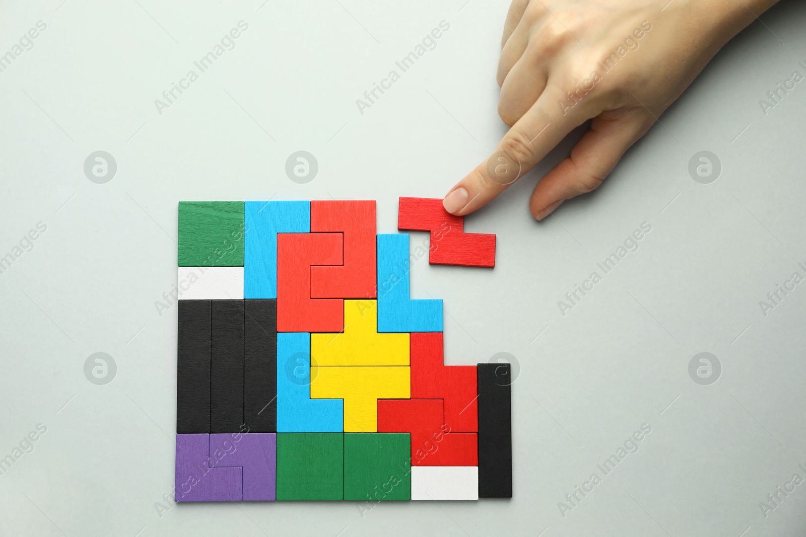 Photo of Woman playing with colorful wooden puzzle pieces on light grey background, top view