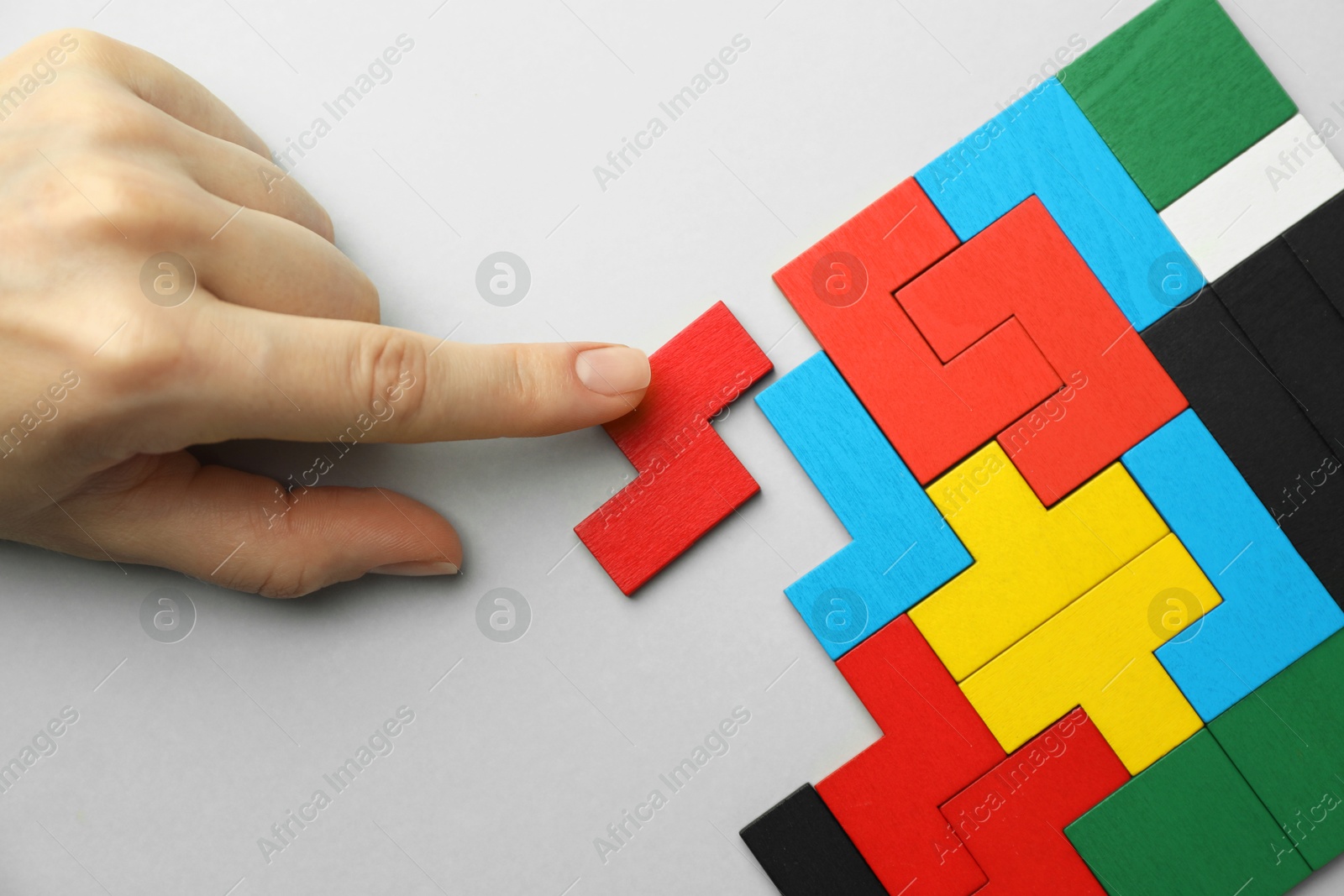 Photo of Woman playing with colorful wooden puzzle pieces on light grey background, top view