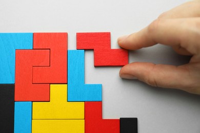 Woman playing with colorful wooden puzzle pieces on light grey background, top view