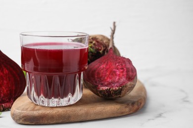 Photo of Fresh beet juice in glass and ripe vegetables on white marble table, closeup. Space for text