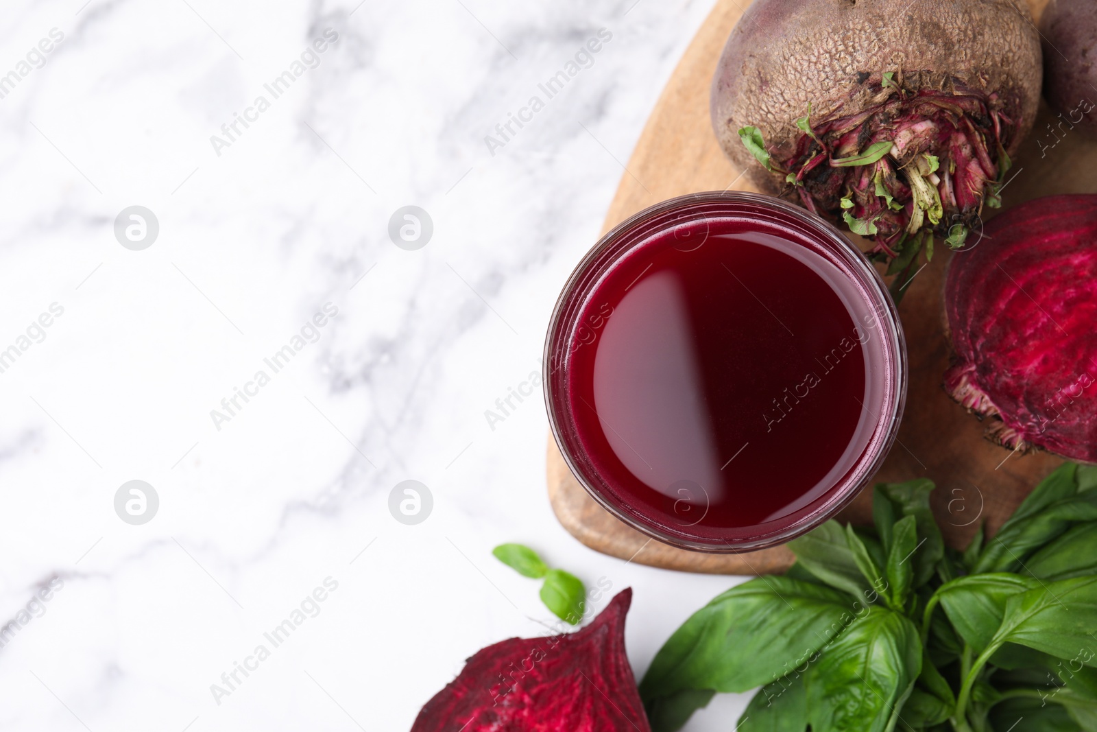 Photo of Fresh beet juice in glass, ripe vegetables and basil on white marble table, flat lay. Space for text