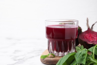 Photo of Fresh beet juice in glass, ripe vegetables and basil on white table, space for text